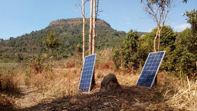 Two small solar panels standing on dry grass, with the flat-topped hill behind