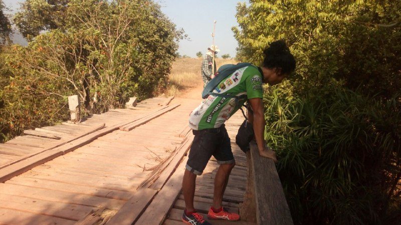 A person leaning on the rail of an old wooden plank bridge, looking down at the water
